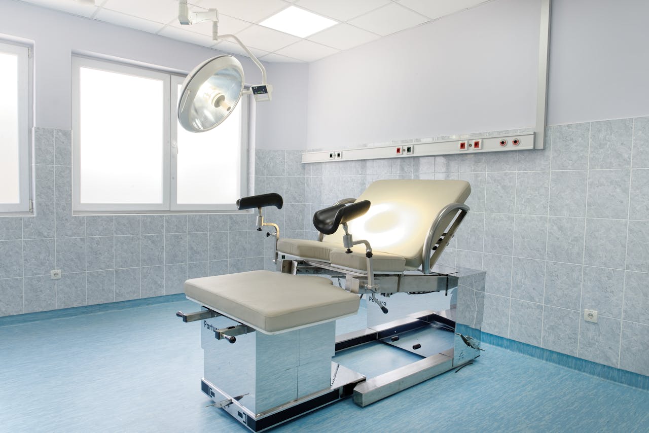 Bright gynecological examination room with adjustable chair and overhead light in a medical facility.